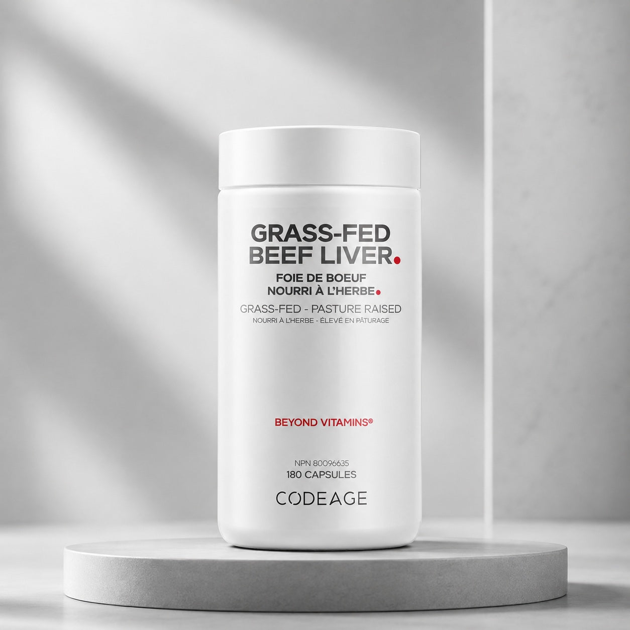 A white bottle of Codeage Grass-Fed Beef Liver capsules displayed on a round gray pedestal against a light gray background with soft shadow overlays.